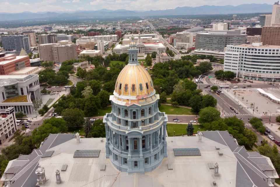 Aerial view of gold Colorado state capitol building with green park and city beyond